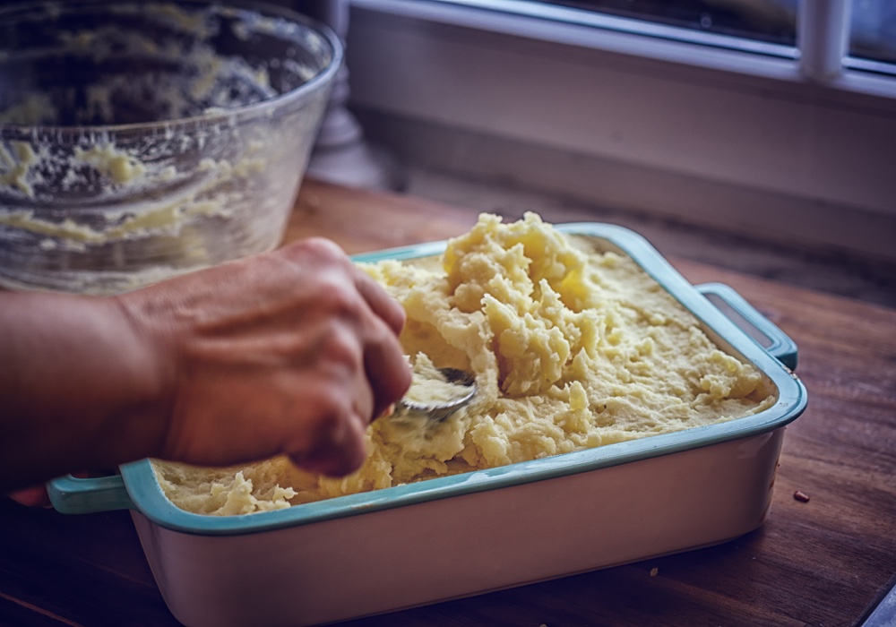 A spoonful of garlic mashed potatoes being lifted from the baking dish.
